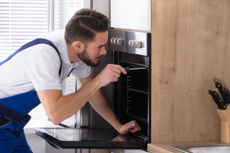 Young,Male,Electrician,Repairing,Oven,With,Screwdriver,In,Kitchen