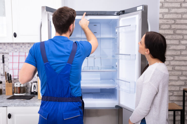 Young,Woman,Looking,At,Male,Serviceman,Checking,Temperature,Of,Refrigerator